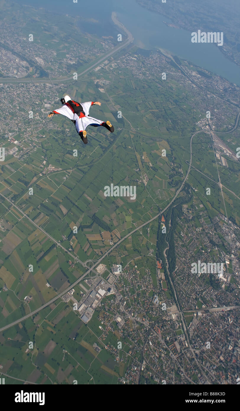 Skydiver fliegt in seinem weißen Wingsuit über eine spektakuläre Landschaft. Der Taucher ist entlang dem Bergrücken tracking. Stockfoto