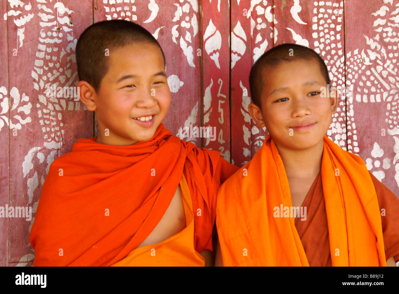 Junge buddhistische Mönche vor bunt bemalten Türen, Wat Xieng Chai Luang, Nam Tha, Laos Stockfoto