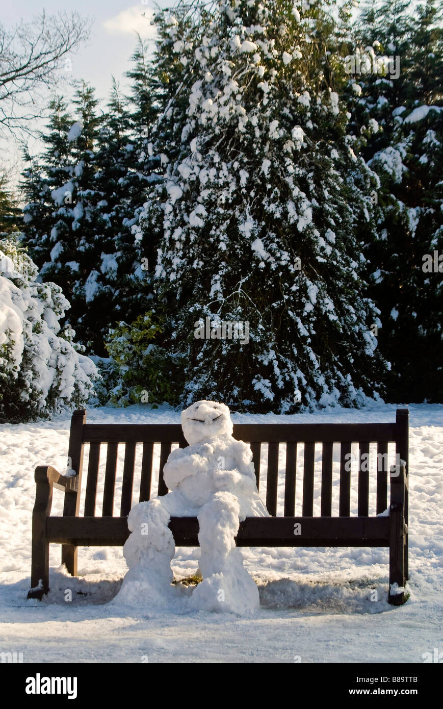 Vertikal nah Porträt eines Schneemannes traditionelle sitzt auf einer Parkbank in der Sonne langsam auftauen Stockfoto