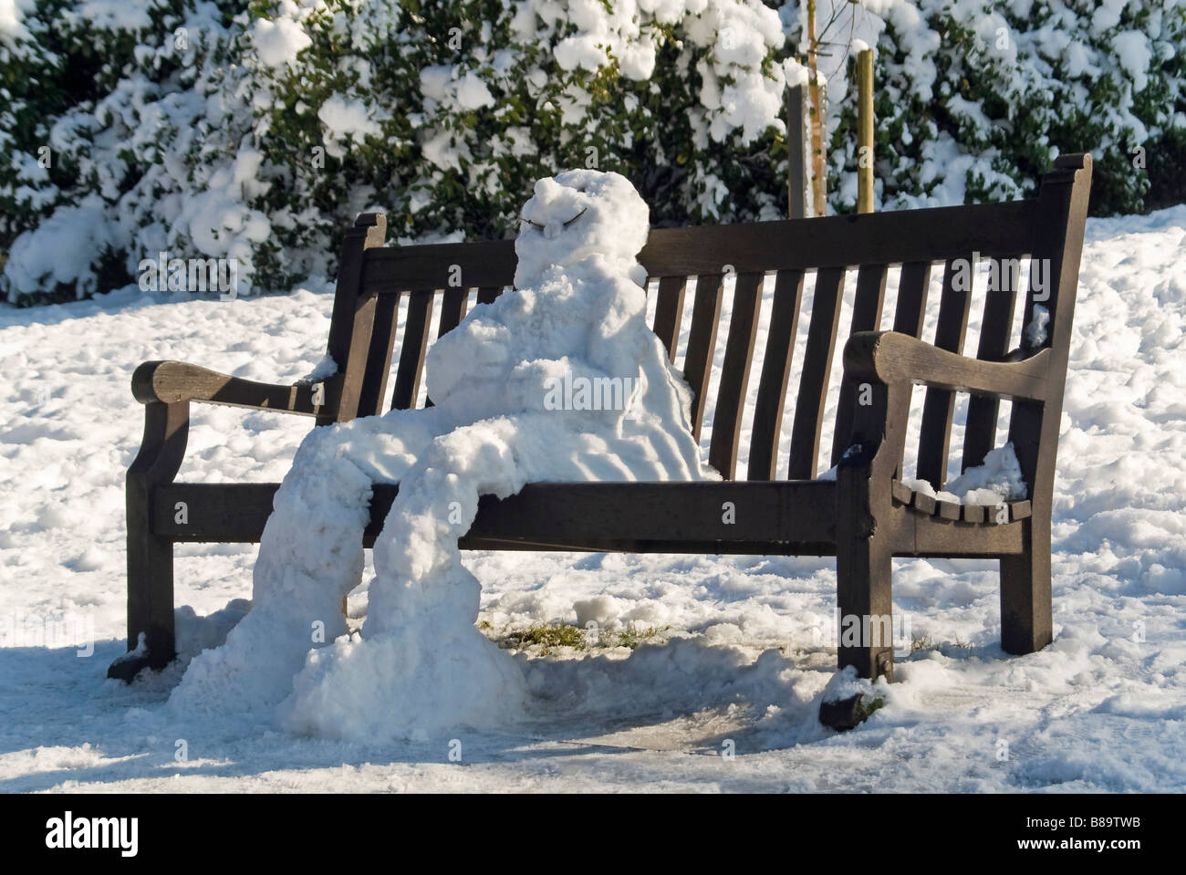 Horizontale nahe Porträt eines Schneemannes traditionelle sitzt auf einer Parkbank in der Sonne langsam auftauen Stockfoto