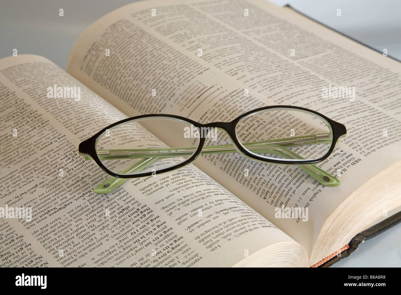Ein paar gemeinsame Brillen oder Brillen liegen auf einem offenen Wörterbuch lesen Stockfoto