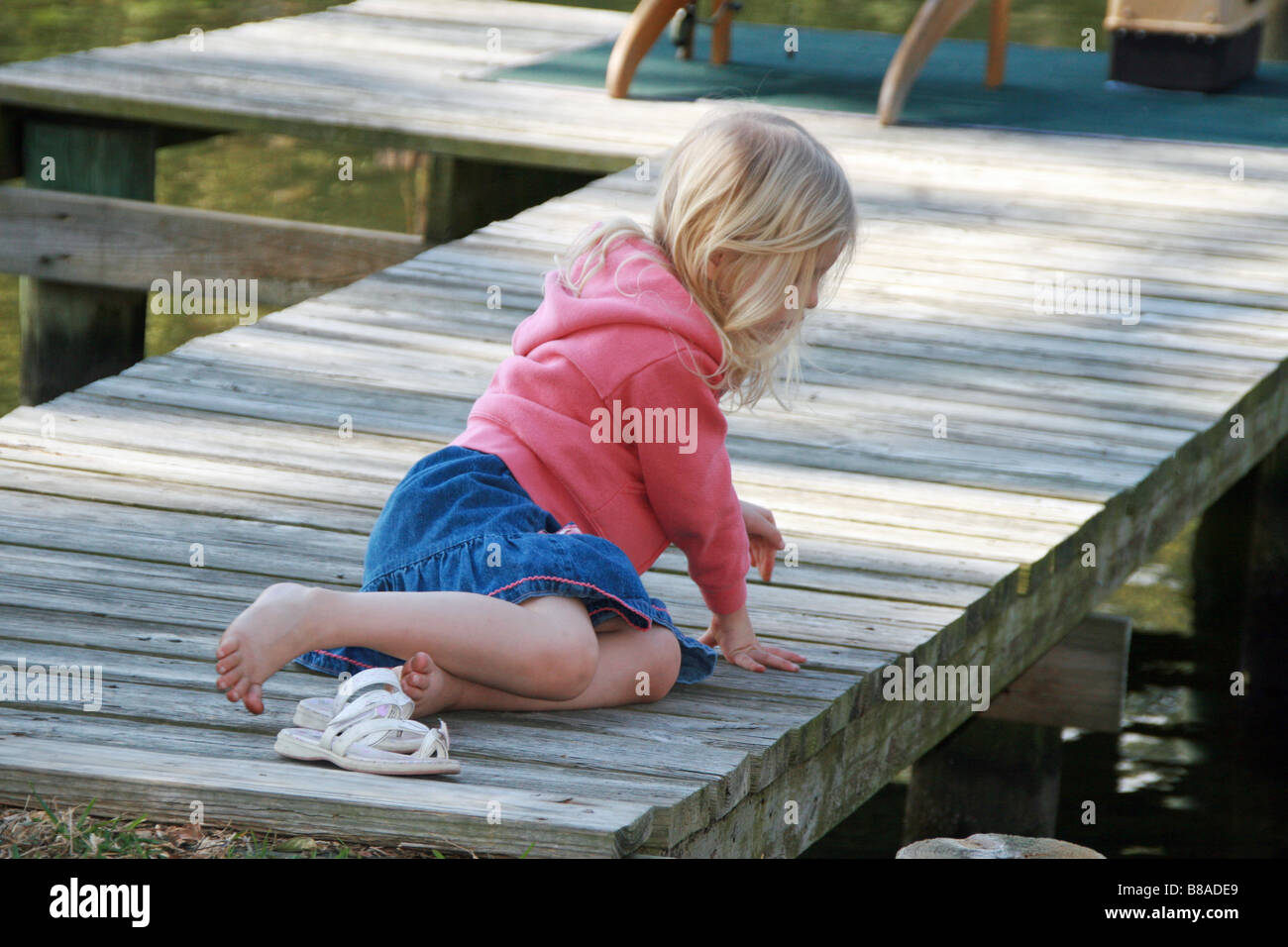 junges blondes Mädchen barfuß auf Holz-dock Blick in Wasser Stockfoto