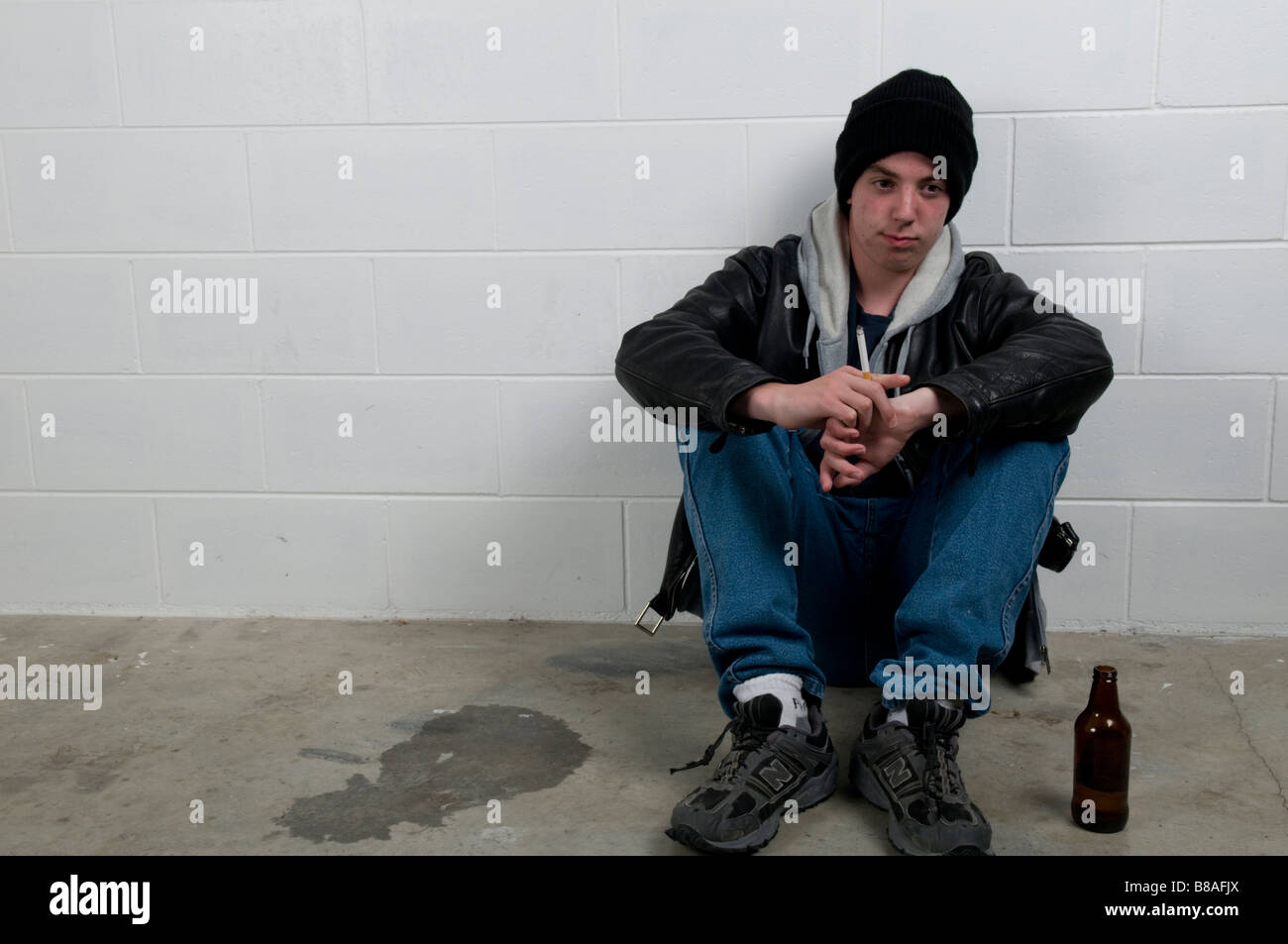 Teenager Junge sitzt mit dem Rücken gegen die Wand, trinken und Rauchen Stockfoto