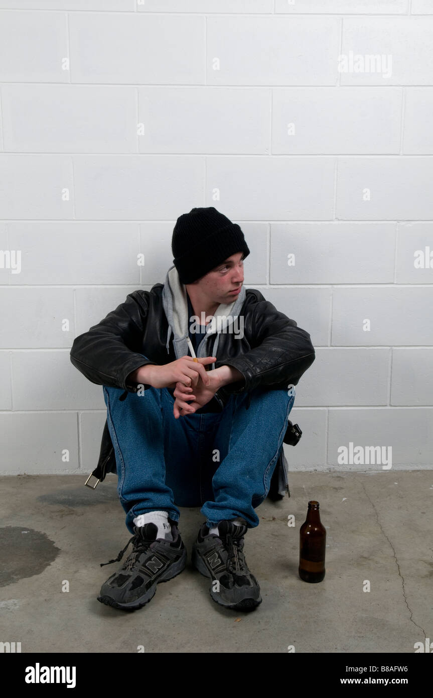 Teenager Junge sitzt mit dem Rücken gegen die Wand, trinken und Rauchen Stockfoto