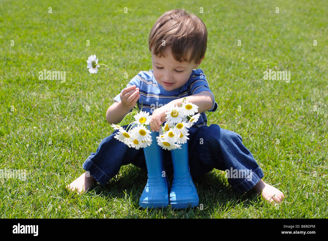 Kleiner Junge platzieren Blumen in Gummistiefeln Stockfoto