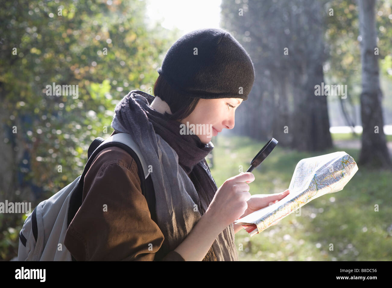 Junge Frau auf der Suche auf Karte mit Lupe, Lächeln Stockfoto
