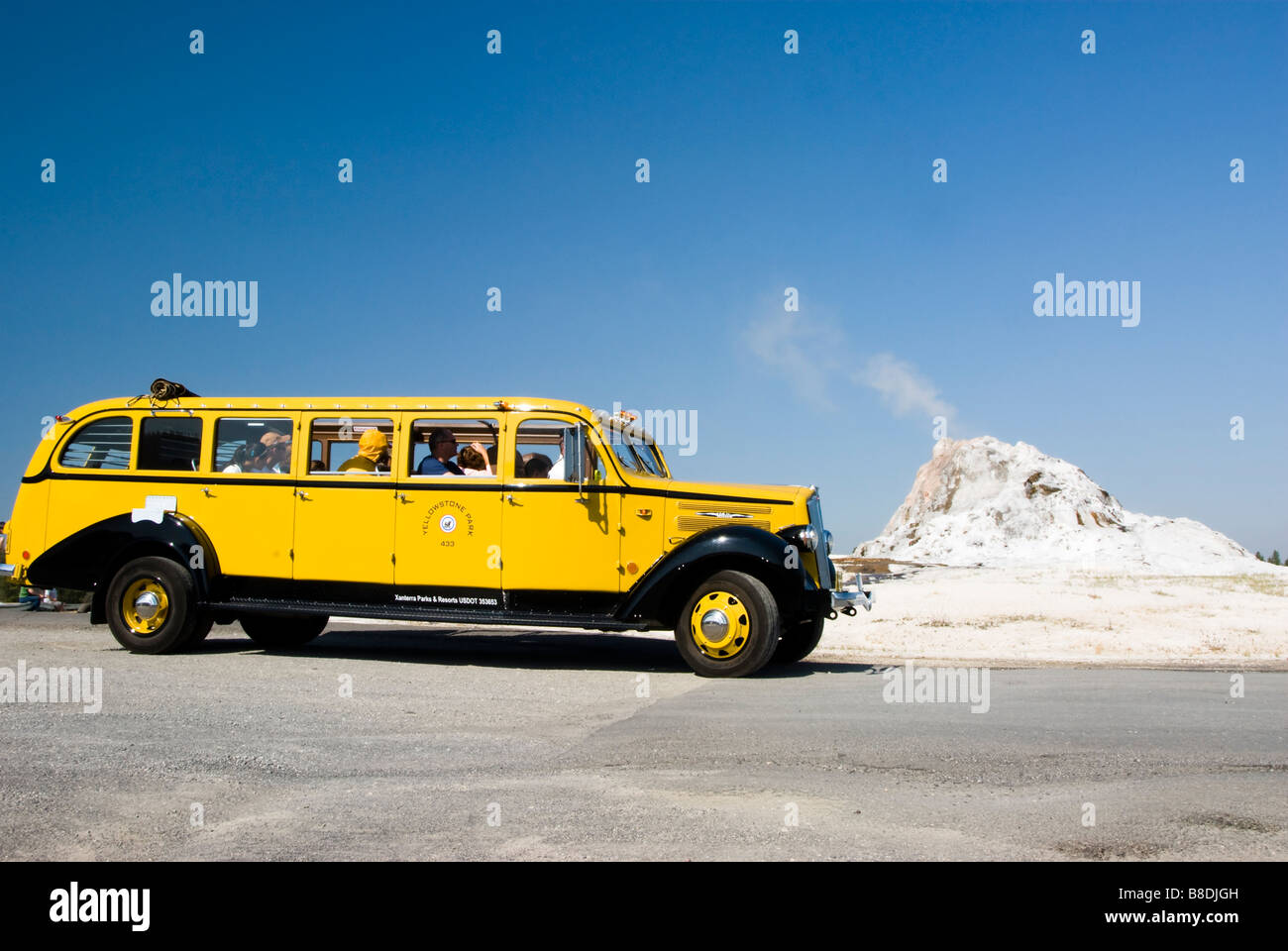 Touristen in eine gelbe Tour Bus beobachten, wie ein Geysir im Yellowstone National Park bricht Stockfoto