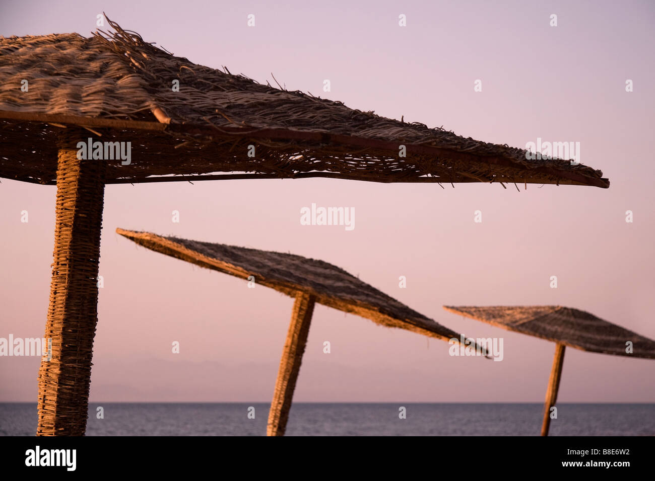 Abstrakte Wicker Sonnenschirme auf einem ägyptischen Strand bei Sonnenaufgang mit dem Roten Meer im Hintergrund Stockfoto