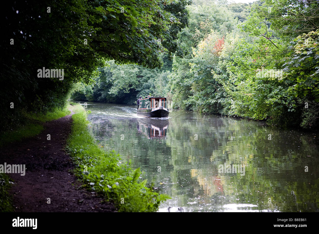 Zwei Männer eine schmale Boot entlang des Bridgewater Kanals zu steuern und eine Lücke in den Bäumen eine Welle des Lichtes fällt zu verhandeln Stockfoto