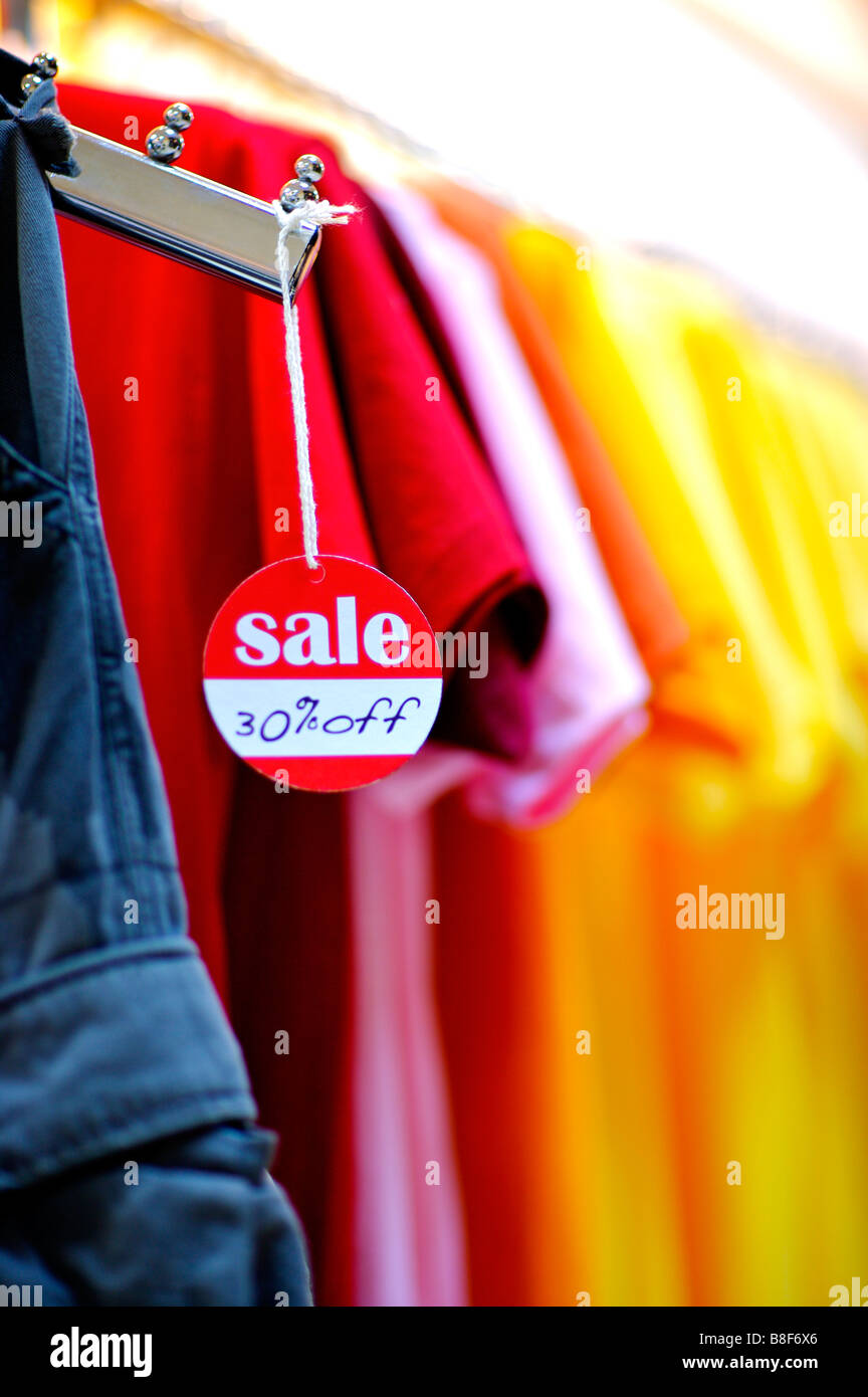 Rote und weiße Verkaufsschild hängend von einem Kleiderbügel vor einer Reihe von bunten t-Shirts Stockfoto
