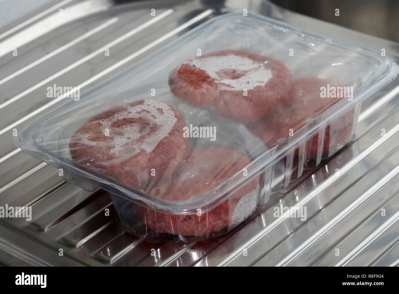 vier Hacksteaks in eine Plastikschale Auftauen bei Raumtemperatur auf einer Küche Spüle Abtropffläche Stockfoto