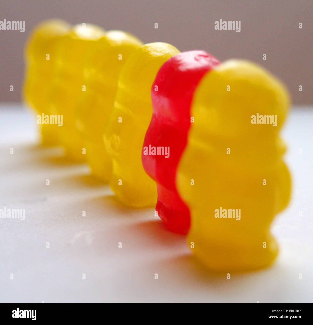 Eine Reihe von gelben Gummibärchen, mit einem einzigen stehen allein rote eine Sekunde von der Front. Stockfoto