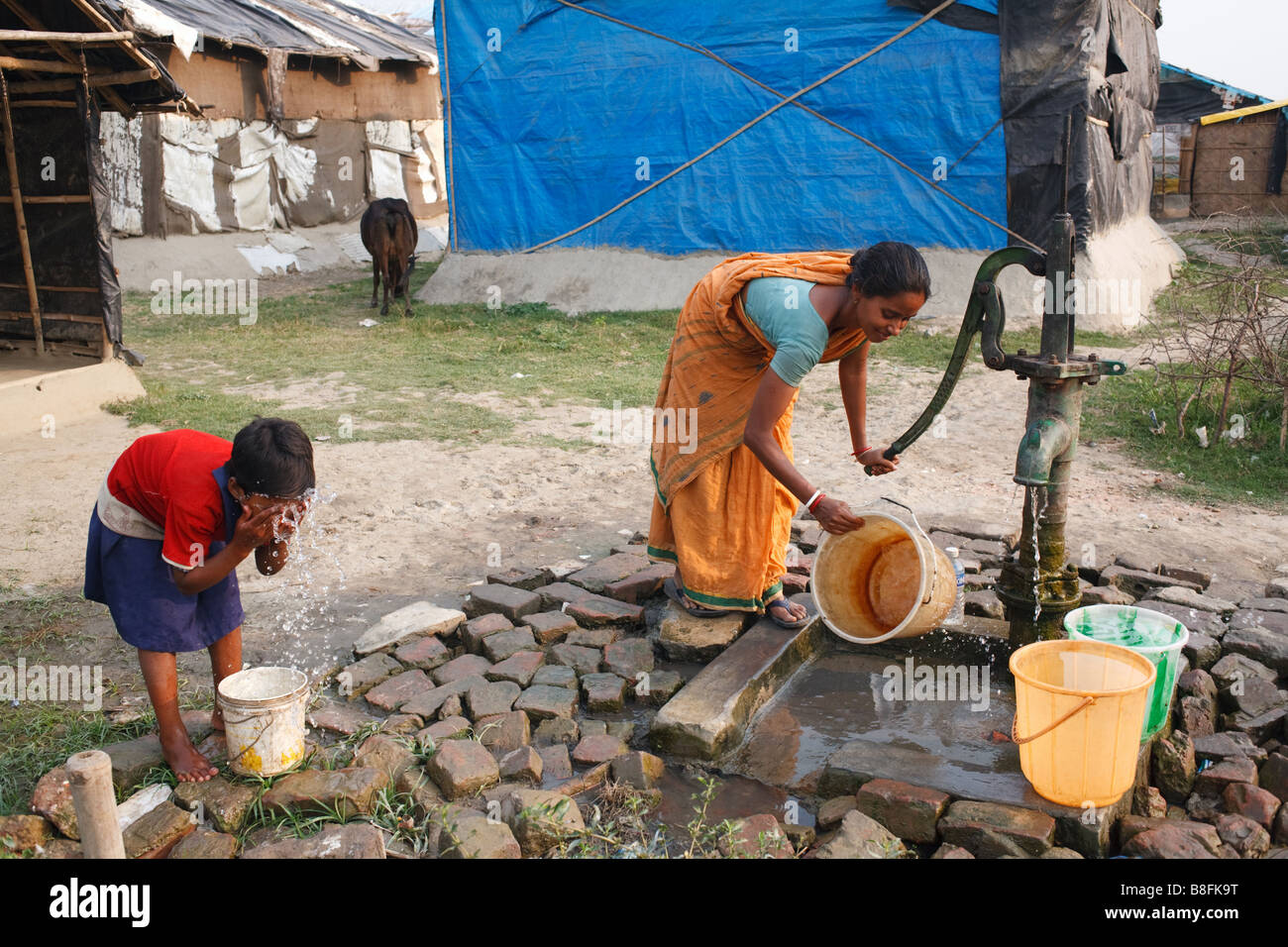 Frau Pumpen Wasser aus dem Bohrloch, während ein junges Mädchen wäscht ihr Gesicht mit Wasser aus dem Eimer in den Slums von Kalkutta, Indien Stockfoto