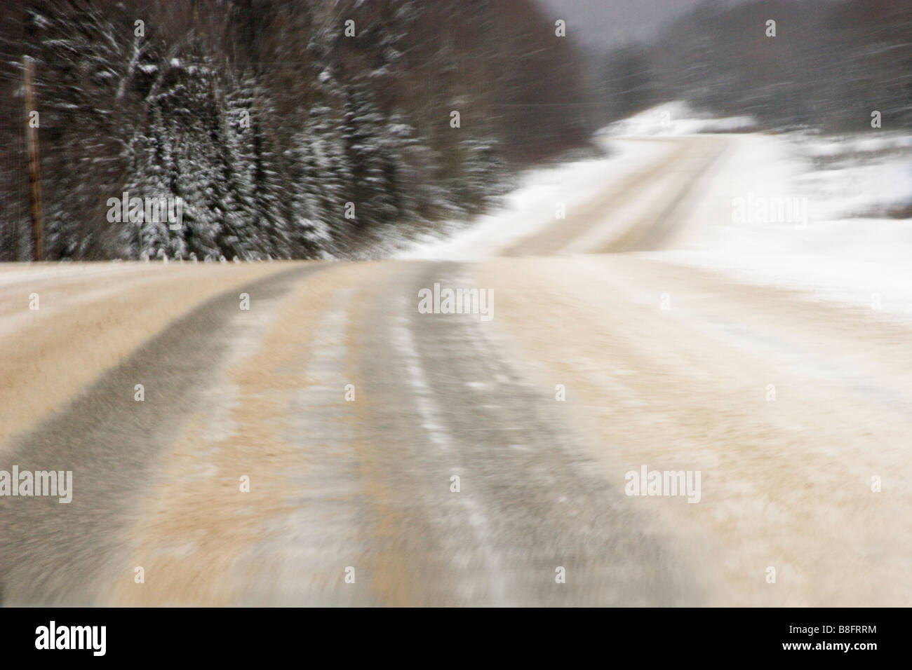Das Bild vermittelt einen Rausch der Geschwindigkeit entlang einer ländlichen, Wicklung, tief verschneiten Bäumen gesäumten Straße tritt in der Ferne im Winter. Stockfoto