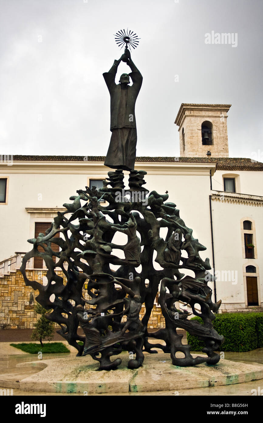 Bronze-Skulptur von Padre Pio in der Mitte der Stadt San Giovanni Rotondo in Italien. Dahinter befindet sich die Kirche von San Leonardo. Stockfoto