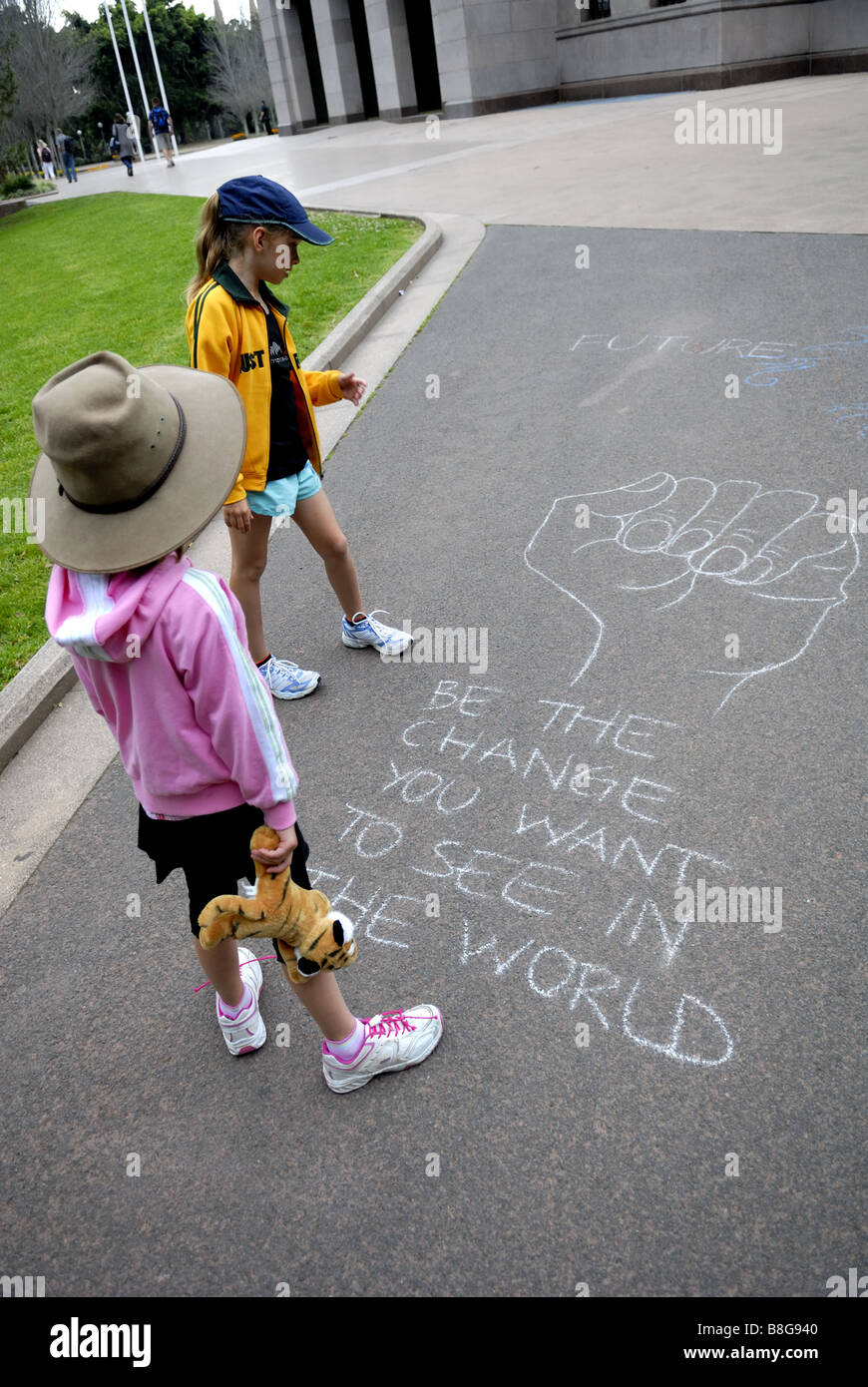 2 Kinder (6 Jahre alt, 10 Jahre alt) lesen, Graffiti, ein Zitat von Mahatma Gandhi, auf Boden angekreidet. Hyde Park, Sydney, Australien Stockfoto