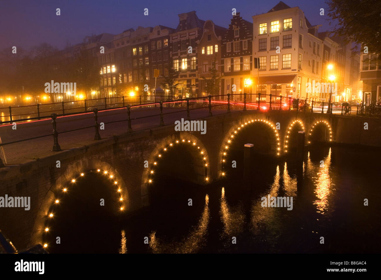 Beleuchtete Brücke spiegelt sich im Kanal in einer nebligen Nacht in Amsterdam Niederlande Stockfoto