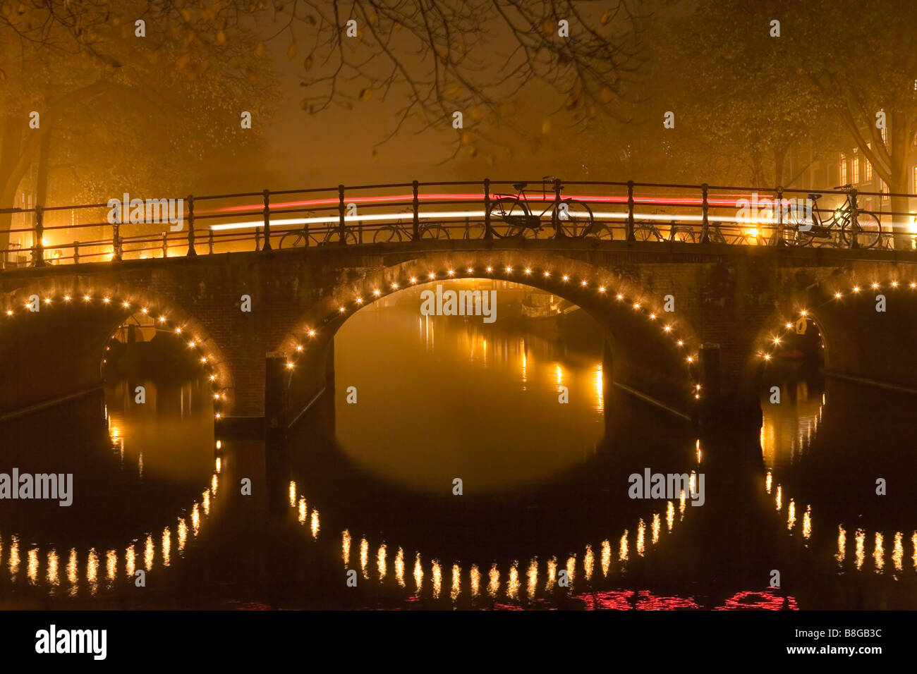 Beleuchtete Brücke spiegelt sich im Kanal in einer nebligen Nacht in Amsterdam Niederlande Stockfoto