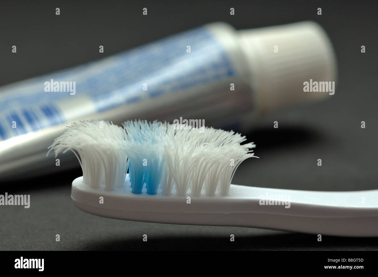 Nahaufnahme einer sehr abgenutzten Zahnbürste mit eine Tube Zahnpasta im Hintergrund Stockfoto
