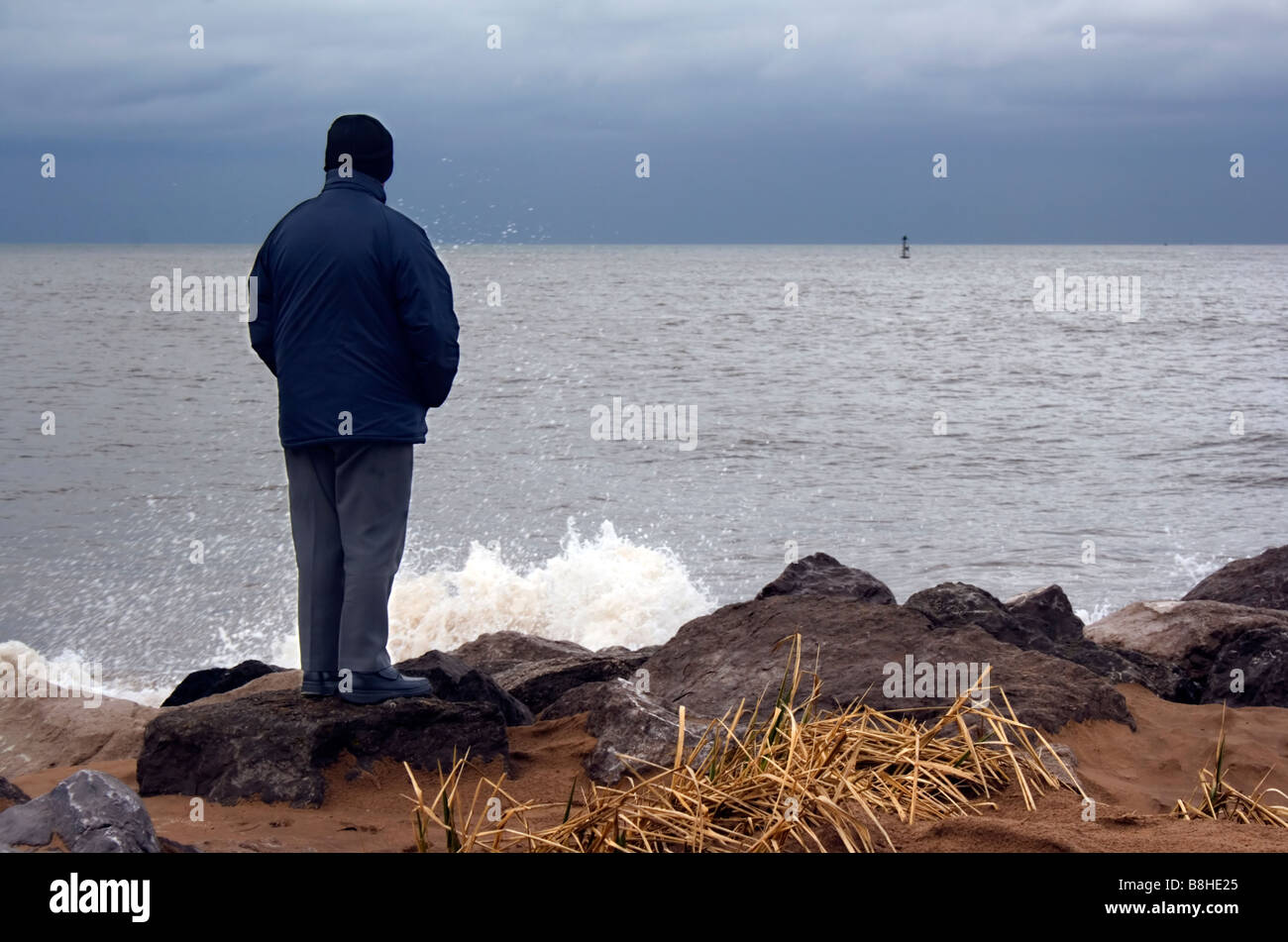 Ein Mann steht auf Felsen mit Blick auf das Meer an einem bitterkalten Wintertag Stockfoto
