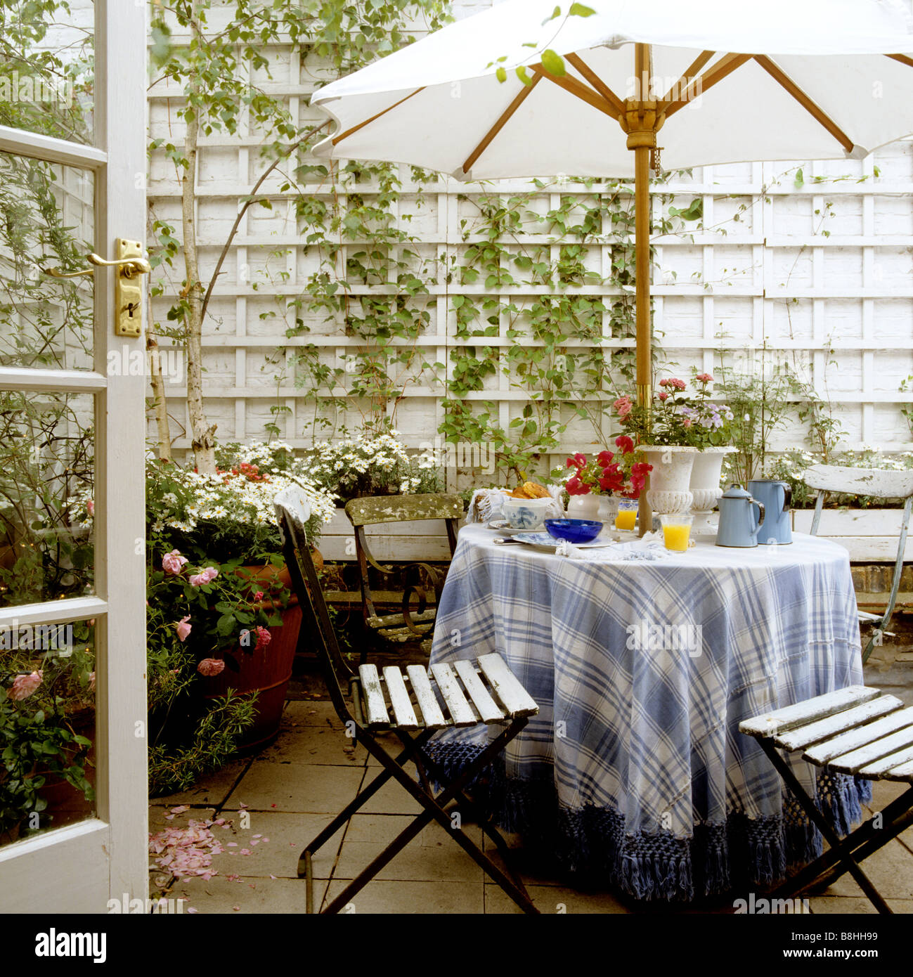 Frühstückstisch mit blau und weiß kariert und Tischdecke mit Fransen und französischen Eisen Café Stühle in einem London-Terrasse-Garten Stockfoto