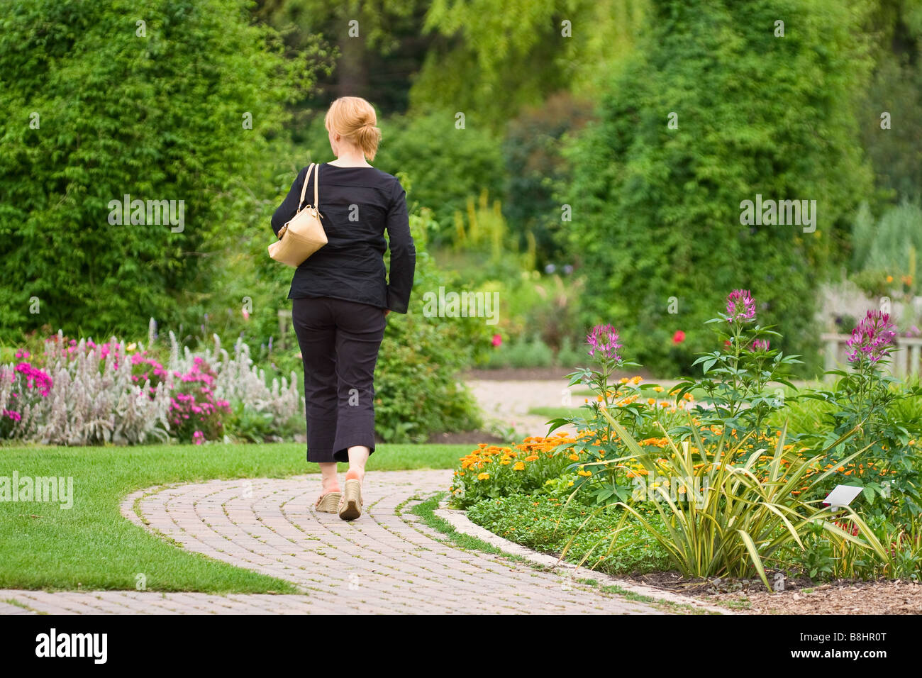 Frau zu Fuß auf verwinkelten Garten Weg, englische Gärten, Assiniboine Park, Winnipeg, Manitoba, Kanada. Stockfoto