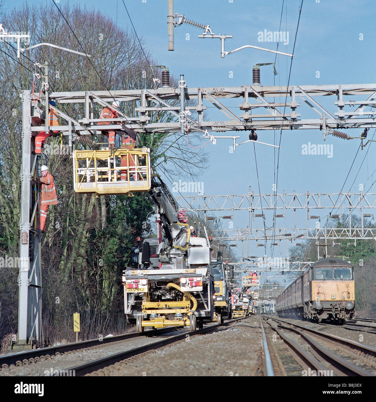 Auftragnehmer auf obenliegende Caternary System hinter teilweise Eisenbahn Blockade, während Züge auf live-Tracks noch ausgeführt werden Stockfoto