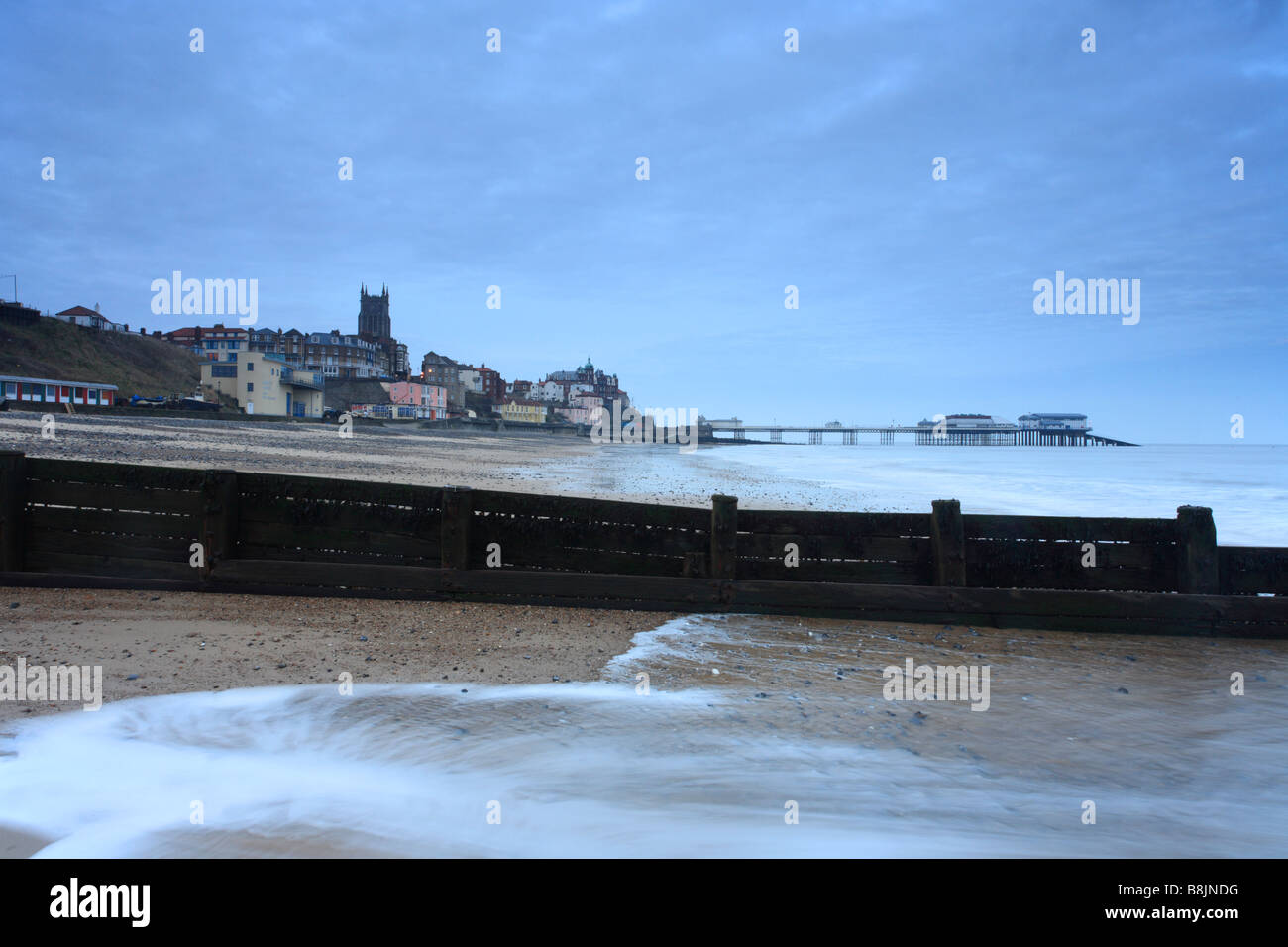 Hölzerne Buhne Cromer Beach, Welle bricht am Ufer, Küstenort Cromer und Pier in der Ferne. Stockfoto