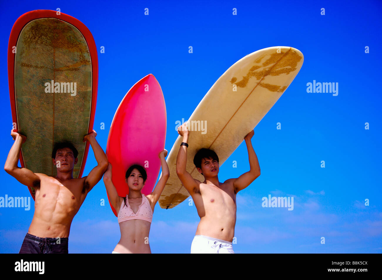 Drei Personen tragen die Surfbretter auf Kopf und wegsehen Stockfoto