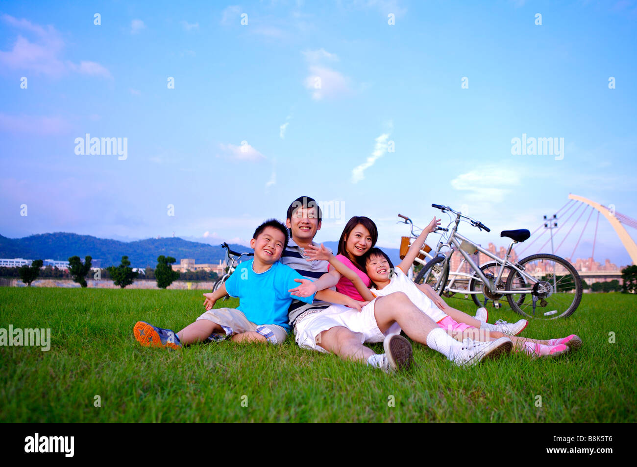 Junge Familie mit zwei Kindern zusammensitzen auf dem Rasen und glücklich lächelnd Stockfoto