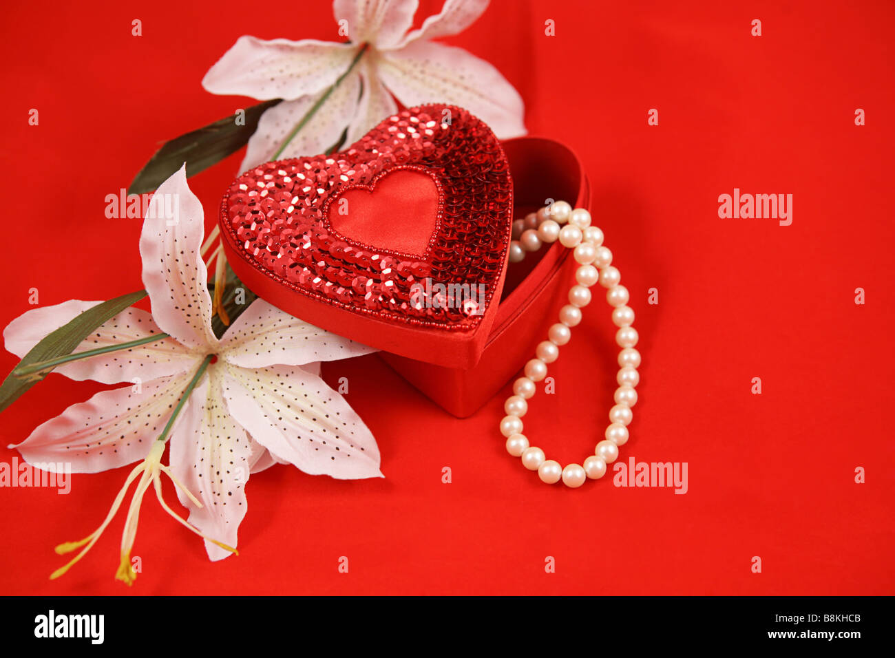 Eine herzförmige Schachtel mit einer Perle Halskette und Ostern Lilien auf rotem Grund Platz für text Stockfoto