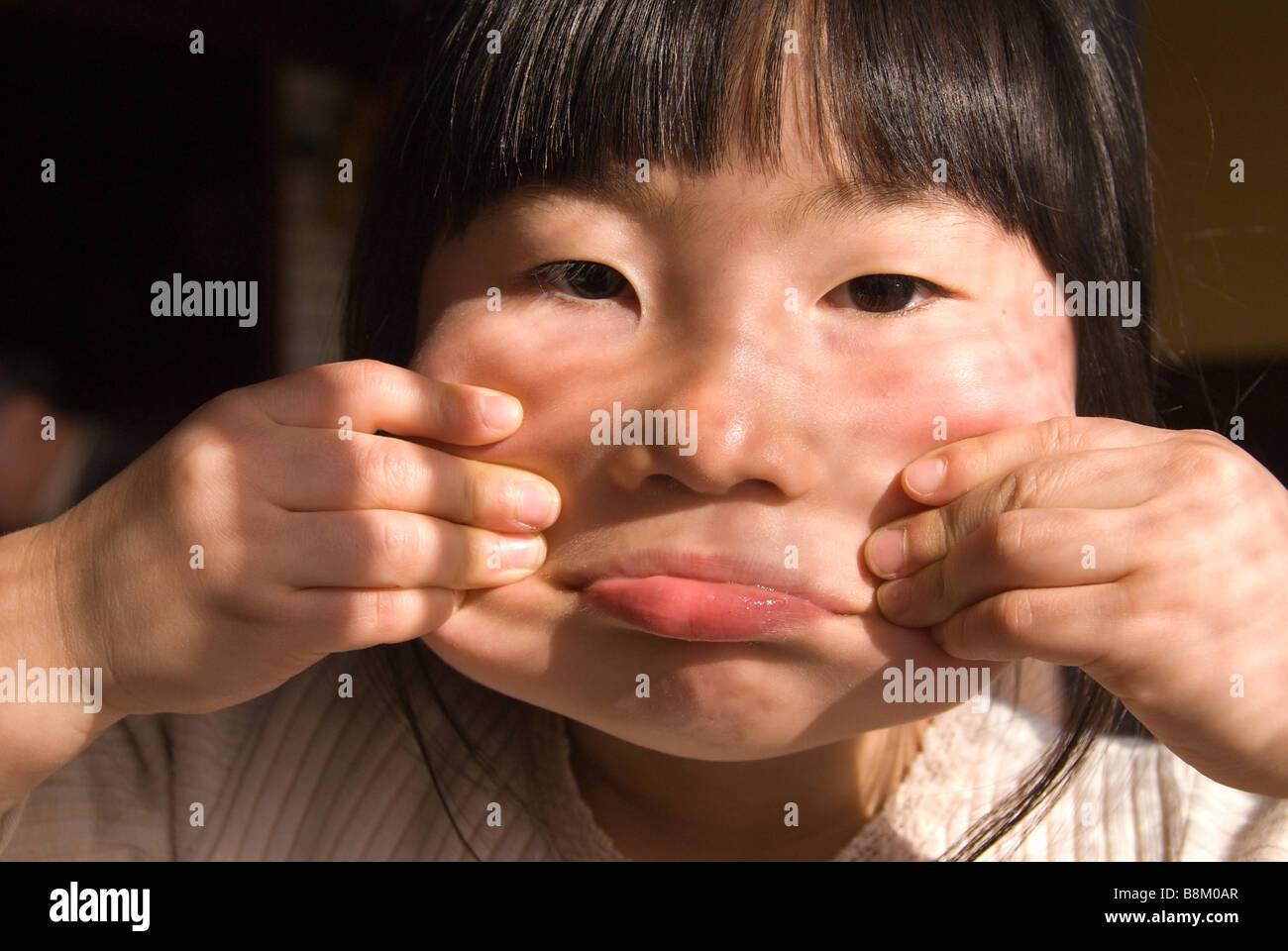 Eine junge Japanerin macht ein Gesicht durch ihre Wangen mit ihren Fingern herausziehen Stockfoto