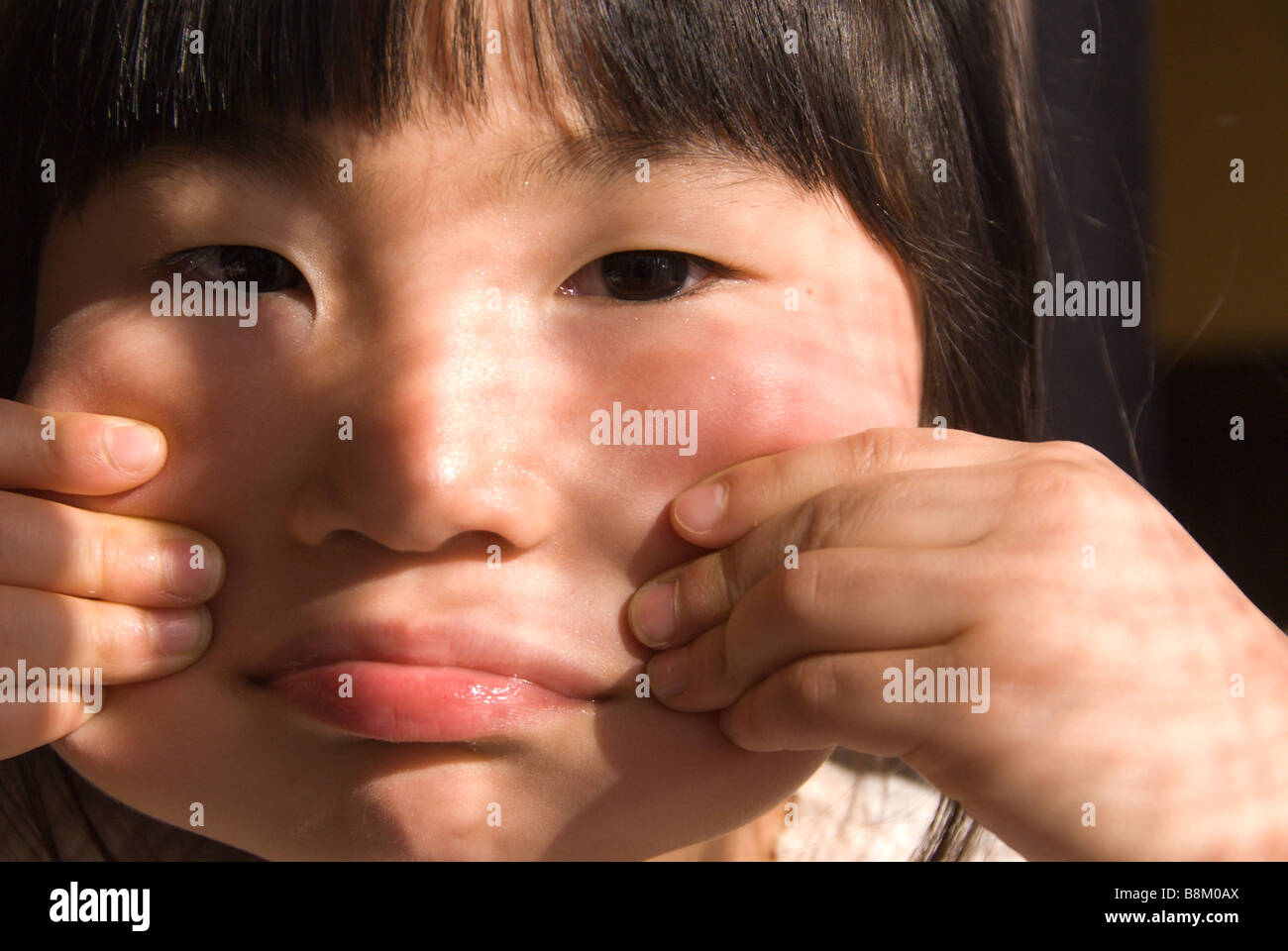 Eine junge Japanerin macht ein Gesicht durch ihre Wangen mit ihren Fingern herausziehen Stockfoto