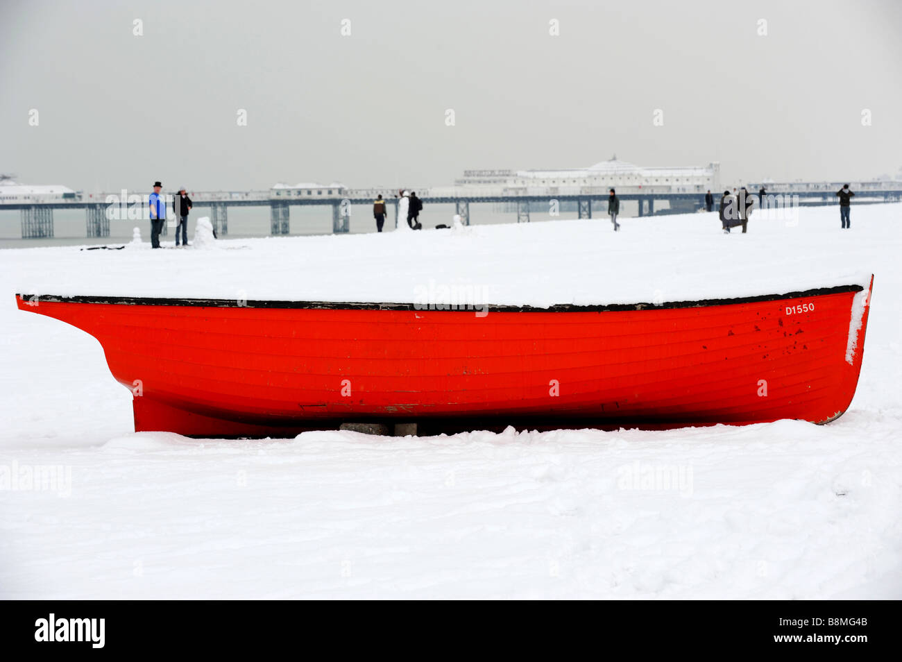 Ein kleines rotes Angelboot/Fischerboot am Strand von Brighton als Schnee fallen weiterhin Stockfoto
