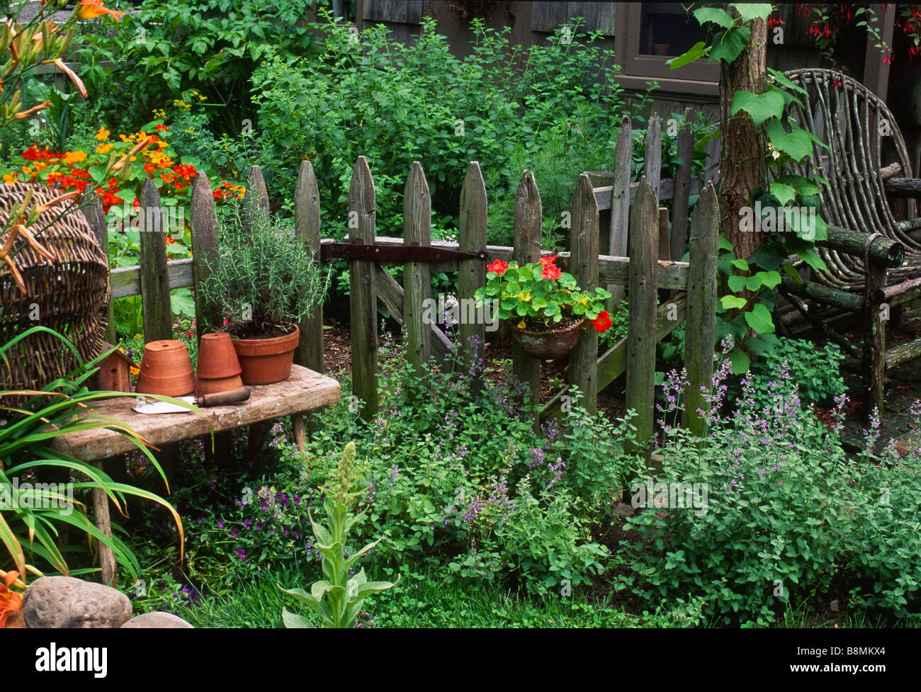 Gartenartikel, einschließlich eine eingemachte Rosmarin ruhen auf einer rustikalen Bank vor einem verwitterten Zaun in einen Garten. Stockfoto