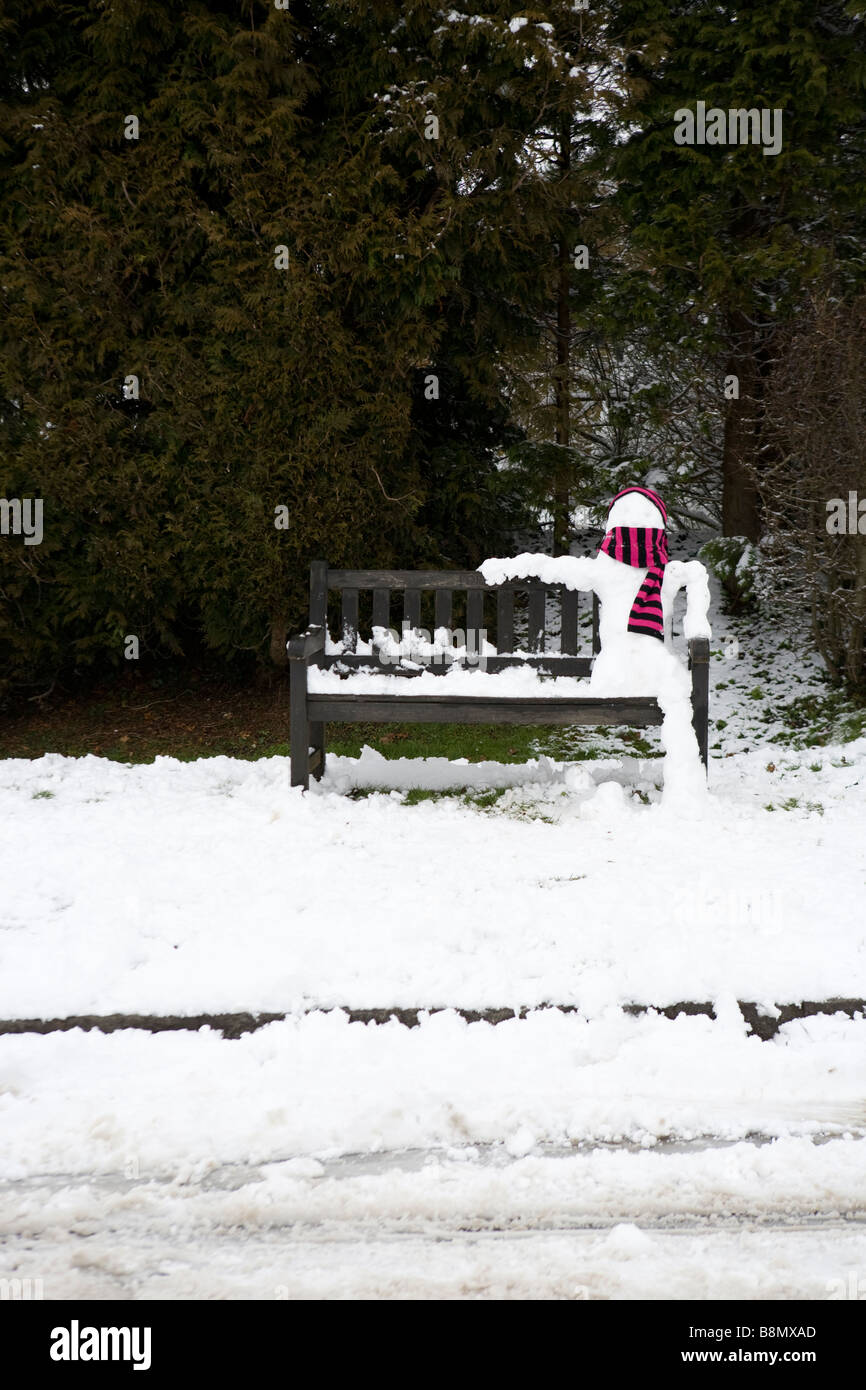 Schneemann trägt einen Schal sitzt entspannt auf einer Bank, die Wartezeit auf den bus Stockfoto