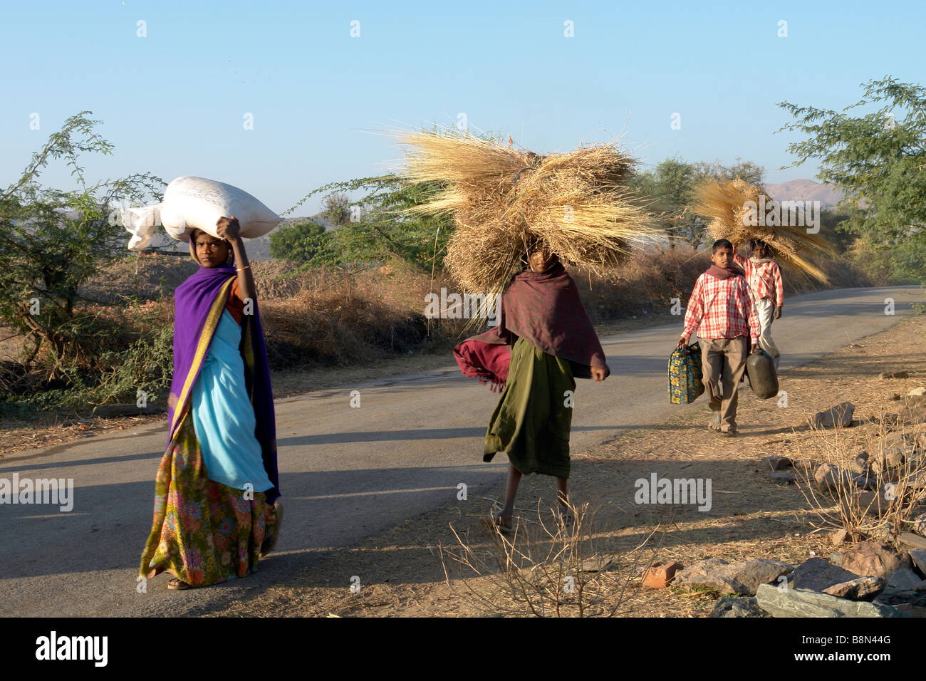 indische Frau in einer ländlichen Gegend mit Produkten und waren auf dem Kopf zu Fuß auf einer Dorfstraße Stockfoto