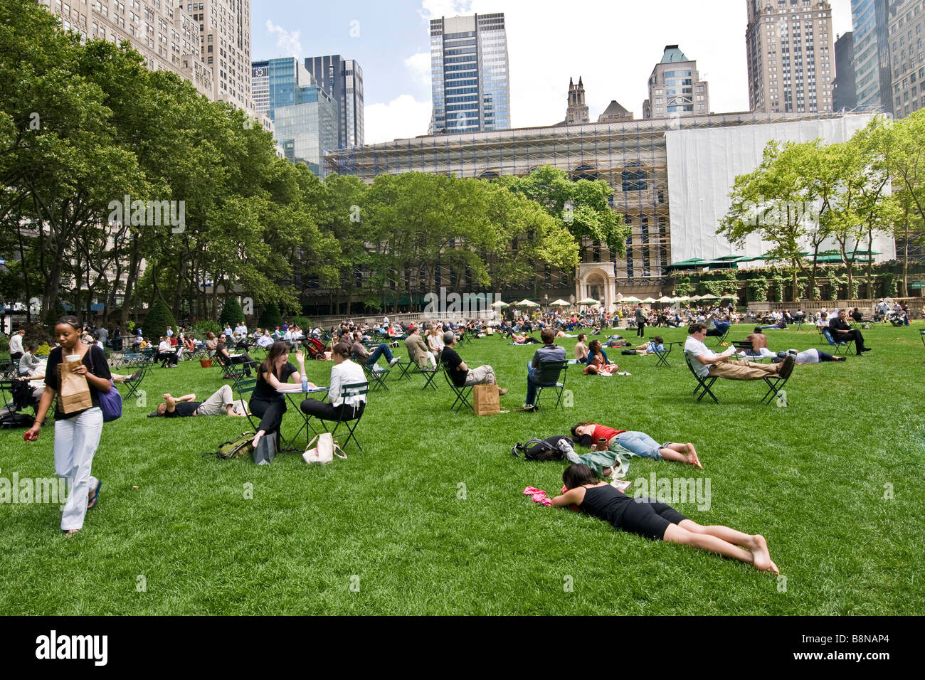 Menschen sitzen auf Stühlen und entspannen auf dem Rasen in einem öffentlichen Garten Stockfoto
