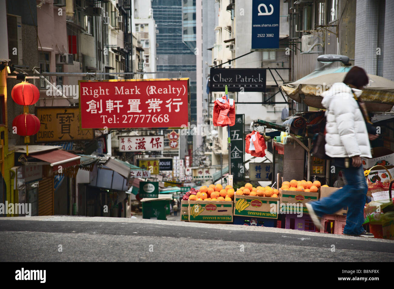 Frau überqueren einer Straße in Hong Kong Straße vorbei an bunten Zeichen und Obststand Stockfoto