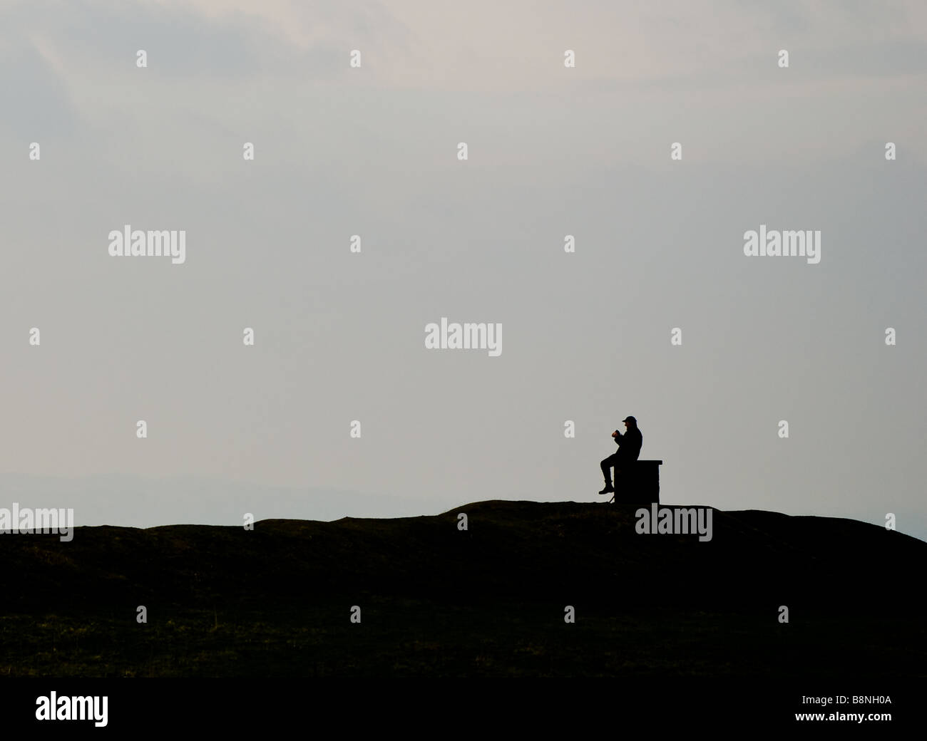 Ein Mann zündet sich eine Zigarette wie er sitzt und die Aussicht vom Burrough Hill in Leicestershire genießt Stockfoto