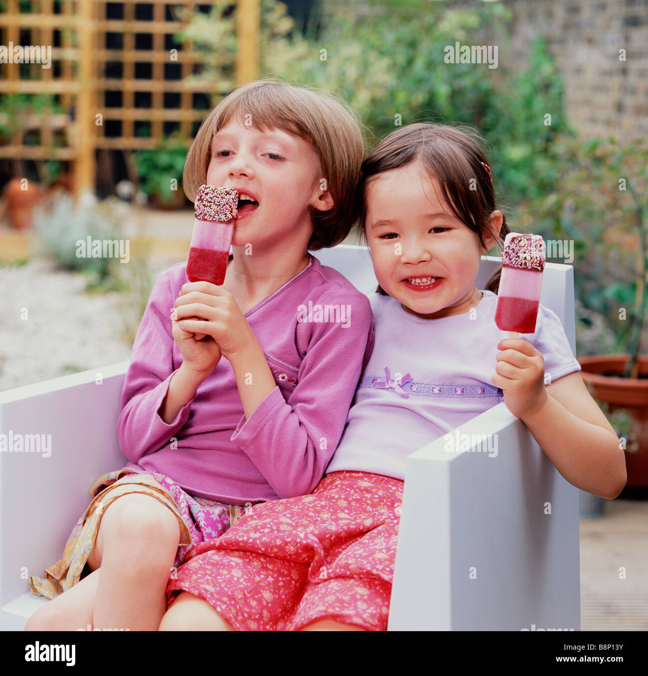 zwei Mädchen essen Eis am Stiehl im Garten Stockfoto
