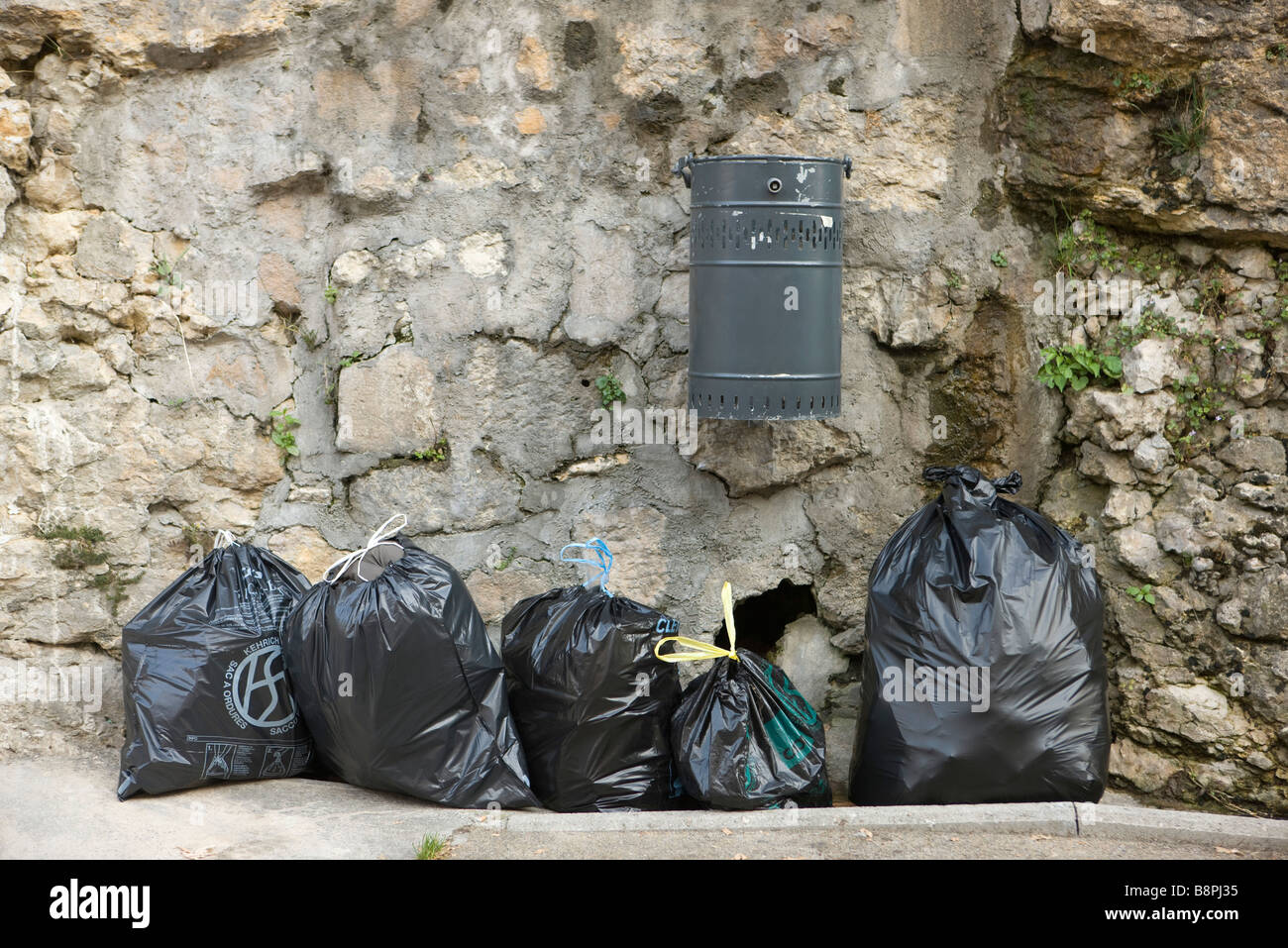 Mehrere Taschen von Müll aufgereiht entlang Steinmauer unter montierten Mülleimer Stockfoto
