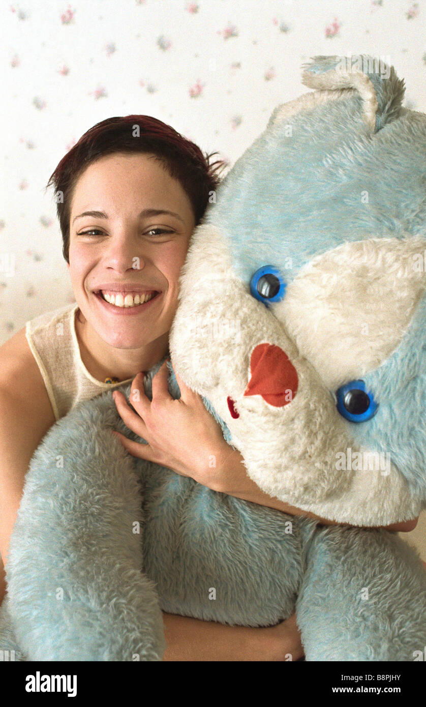 Junge Frau umarmt Teddybär lächelnd in die Kamera Stockfoto