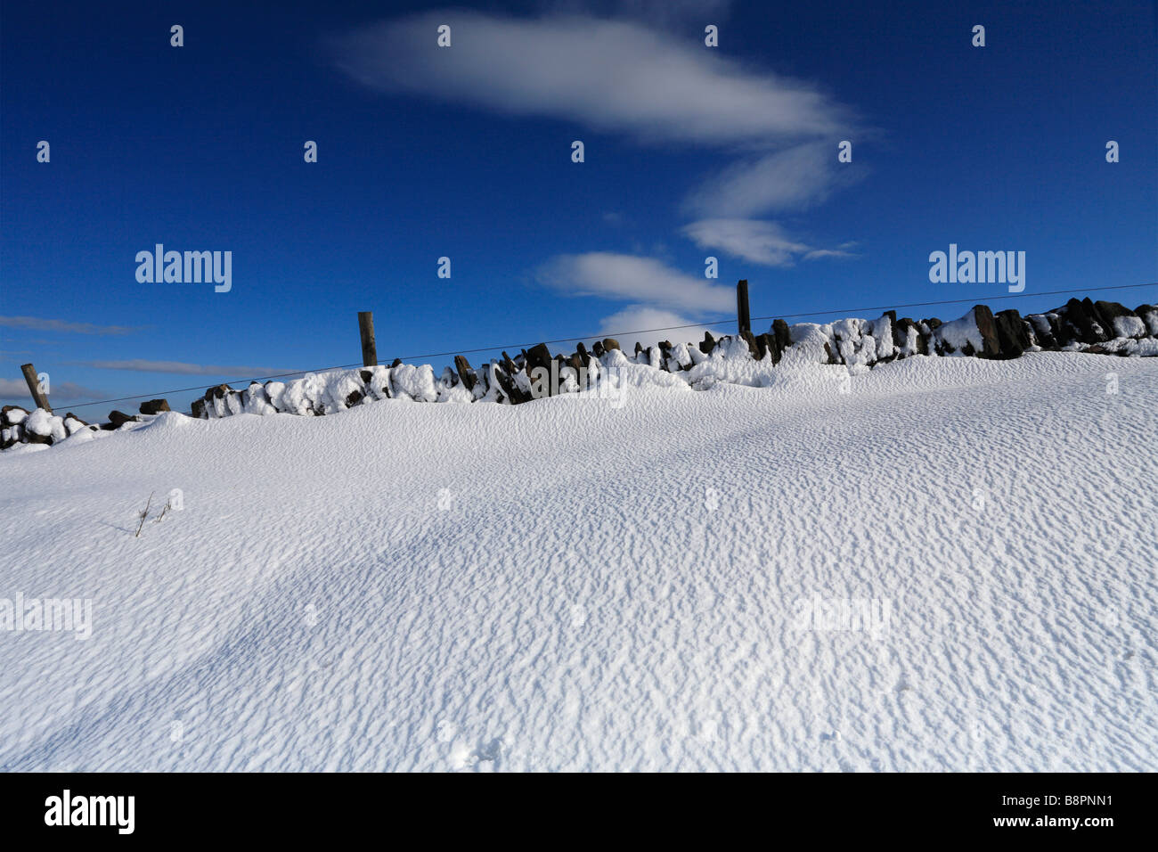 Eine Snow Drift gegen eine Trockenmauer oben Meltham, West Yorkshire, Peak District National Park, England, UK. Stockfoto