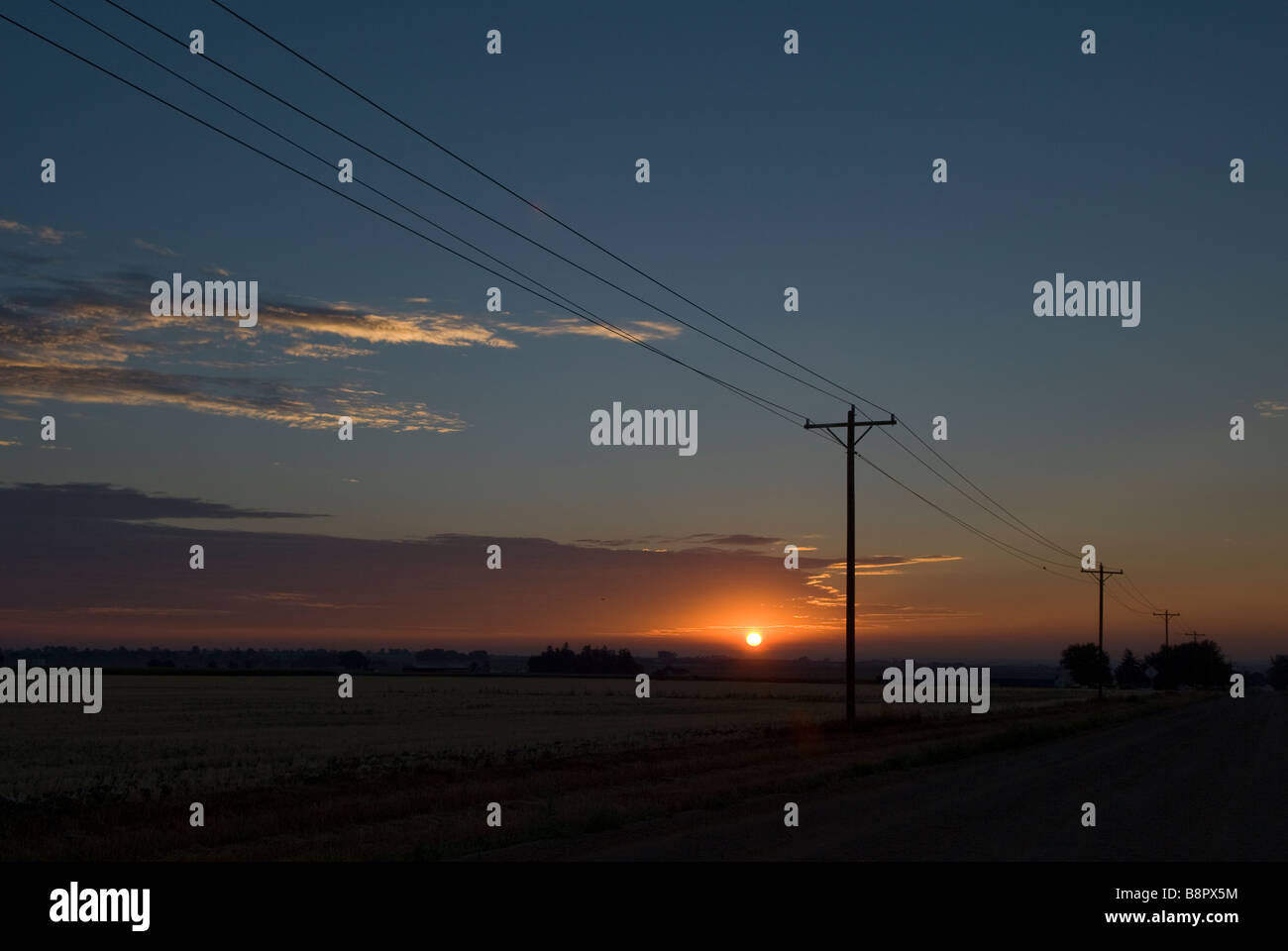 ländliche Sonnenaufgang auf einsamen Landstraße mit Telefonmasten Stockfoto