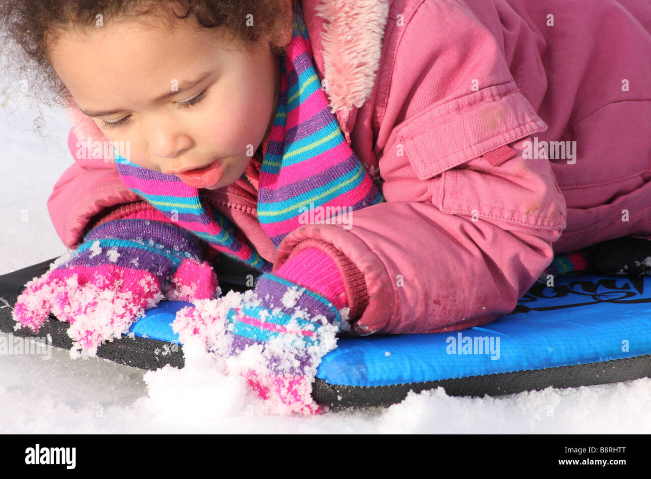 Kleinkind, das kleine Mädchen schwarze ethnische gemischt, Rennen glücklich lächelnde Spaß Schnee Eis rote Spitze junge Stockfoto