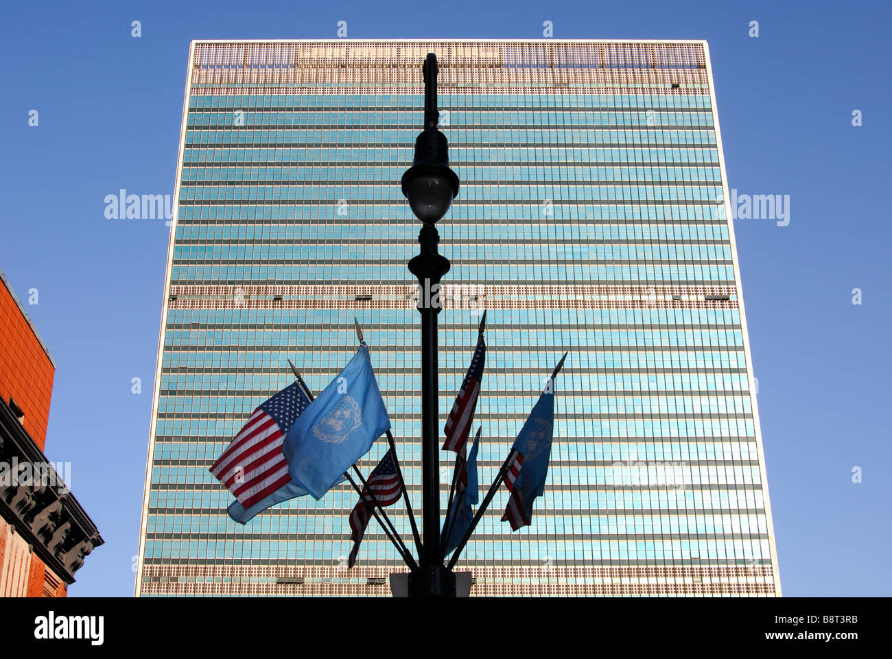 Laternenpfahl mit UN und USA Flaggen vor der Glasfassade der Hauptsitz der Vereinten Nationen, UNO, New York, USA Stockfoto
