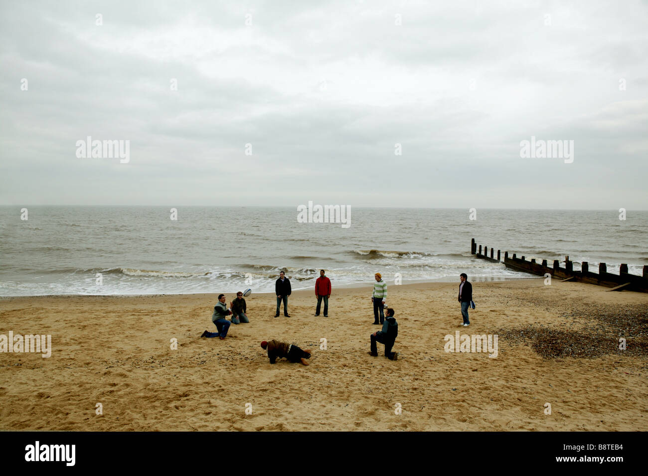 Gruppe junger Männer standen in einem Kreis ein Spiel Ball an einem Sandstrand in den kalten Wintermonaten für Englisch Stockfoto