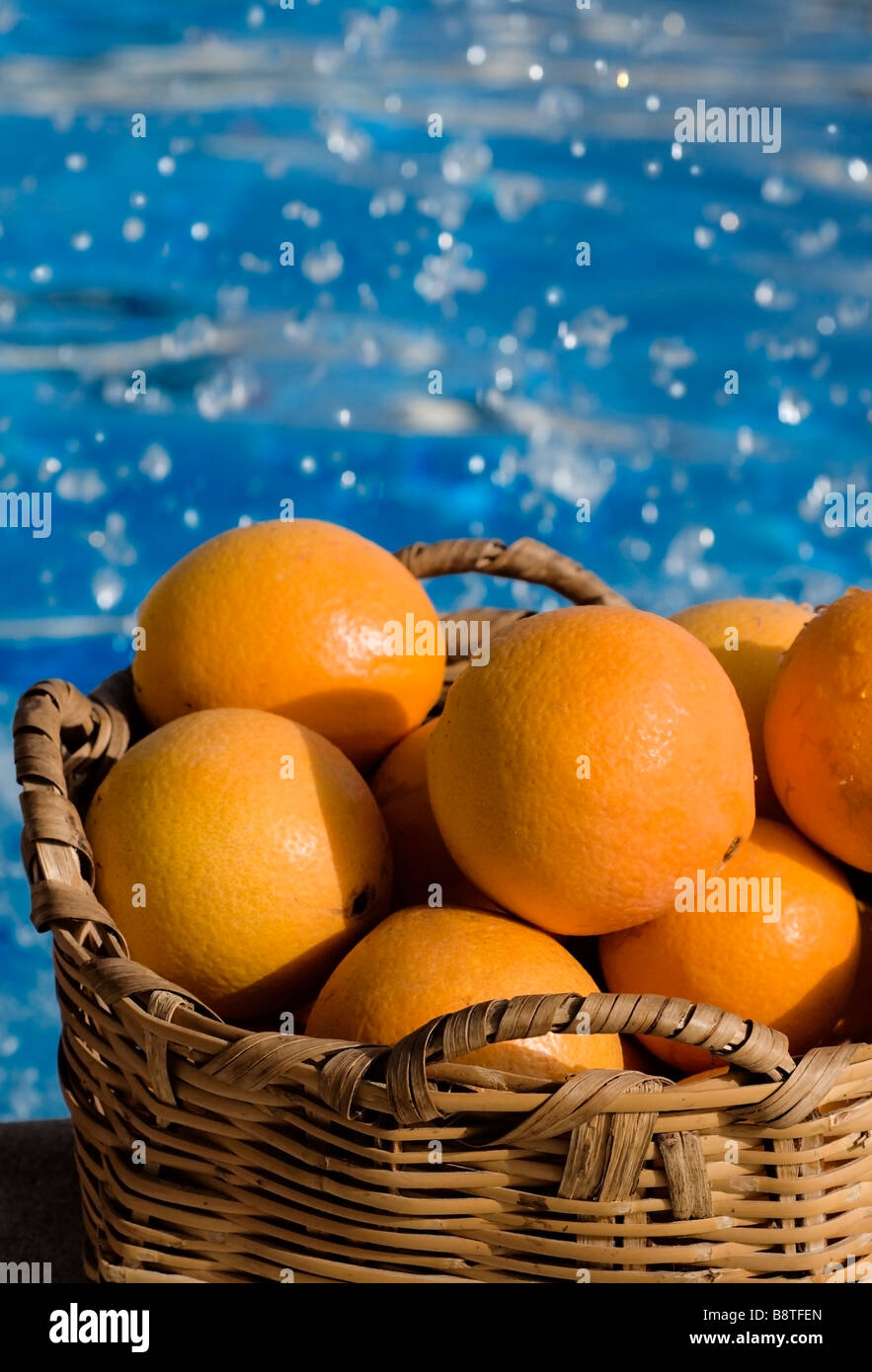 Orangen Warenkorb POOLS SPLASH SUN FRISCHE SPANIEN Korb der sonnigen Spanischen Orangen mit Schwimmbad und Spritzwasser hinter Stockfoto