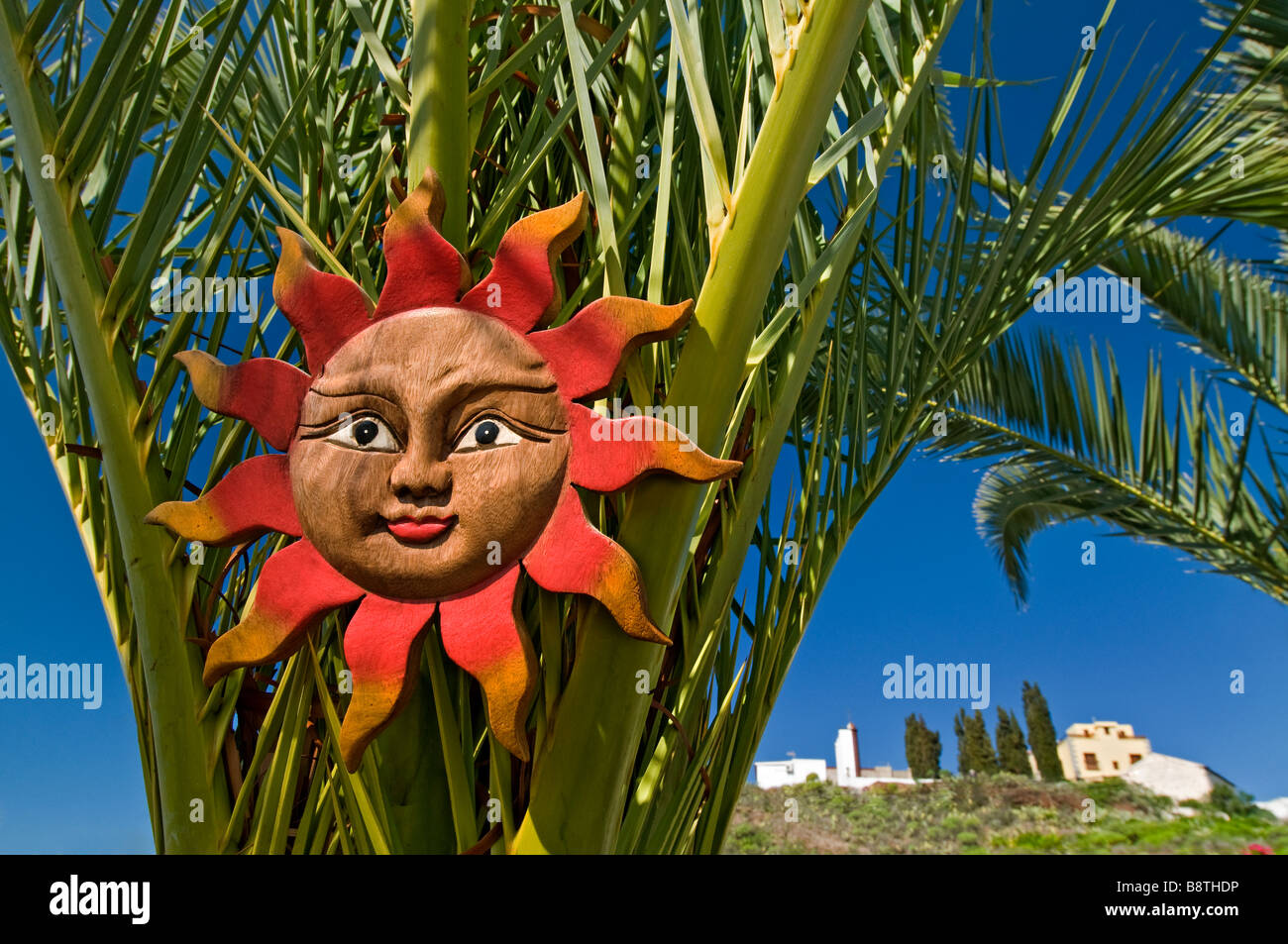 Rustikale geschnitzten hölzernen Sonne Gesicht Plaque hängen an einer Palme als eine Garteneigenschaft in einer Situation, sonnigen Urlaub am Mittelmeer Stockfoto